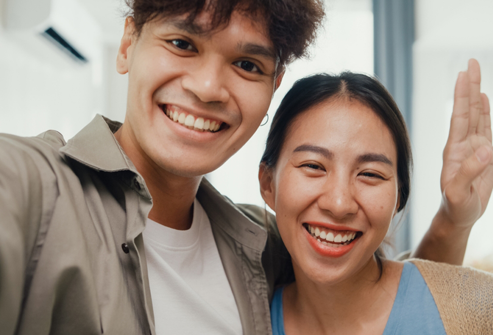 Young couple smiling and waving during a selfie, healthy smiles, Toms River area