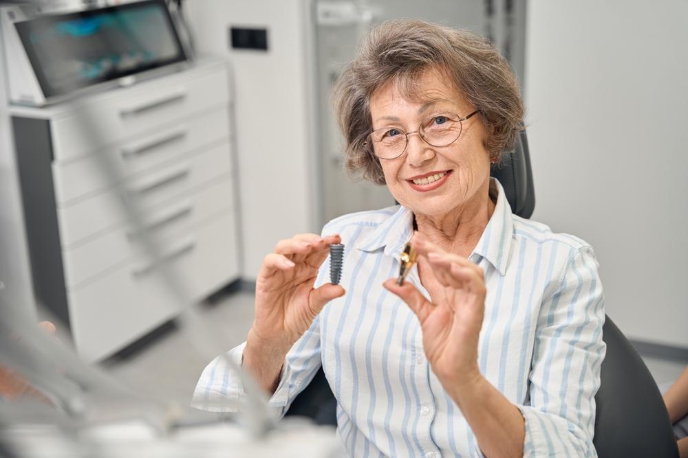 Elderly woman holds model of the components of dental implant