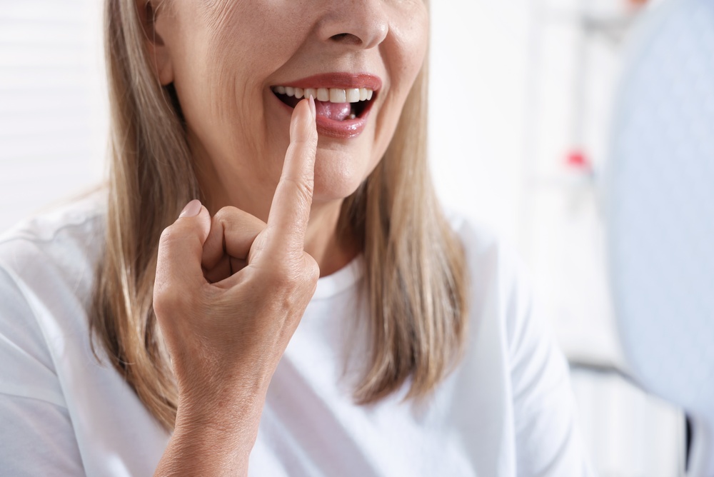 Senior woman looking in mirror at her teeth with dental implant at clinic, closeup