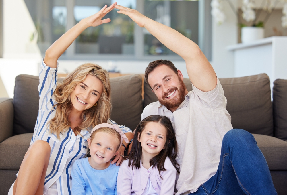 Smiling family of four on a couch, parents' arms forming a roof shape above two daughters, Toms River, NJ 